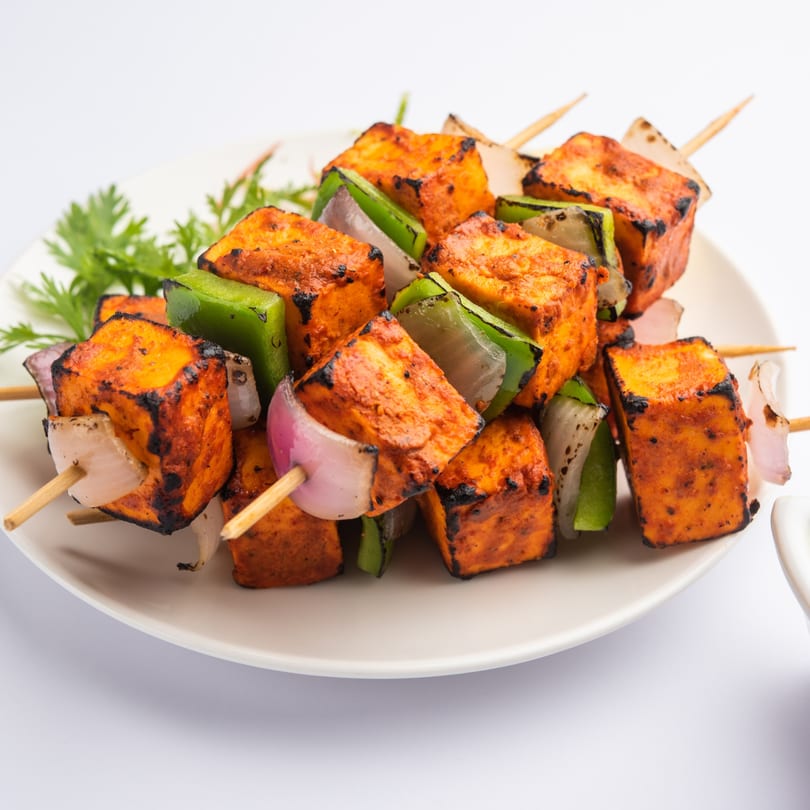 Grilled paneer tikka skewers with bell peppers and onions, garnished with cilantro on a white plate.