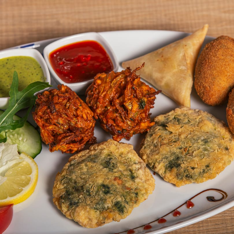 A platter of Dosa South Indian Grill appetizers, including samosas, pakoras, and fried patties with dipping sauces.
