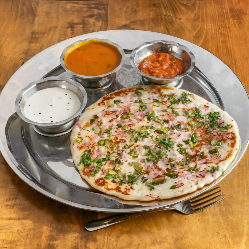 South Indian uttapam with three small bowls of chutneys and sambar on a silver platter.
