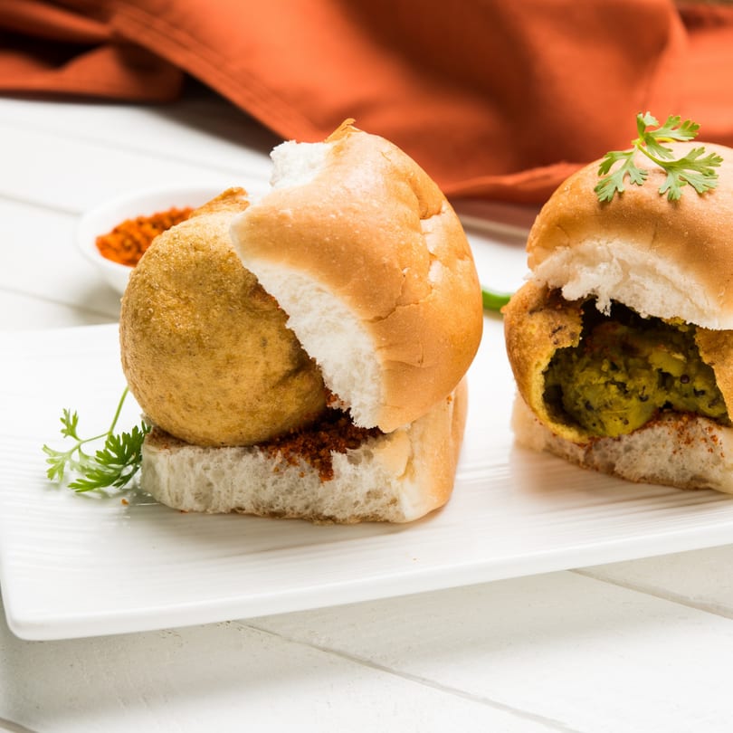 Two vada pavs, one whole and one cut open to show the green filling, on a white plate.